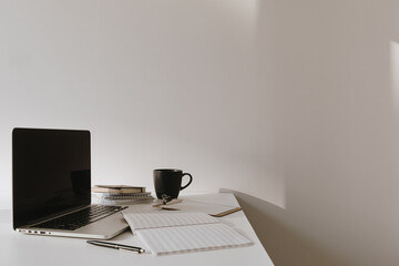 Wall Mural - Laptop on table with coffee cup, paper sheet against white wall. Minimalist home office workspace.
