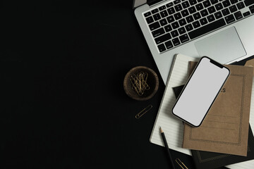 Wall Mural - Flatlay of blank screen mobile smart phone, laptop, notebooks, clips in wooden bowl on black background. Home office desk workspace. Business, work template. Flat lay, top view.