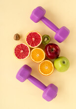 Bright Juicy Halves Of Citrus Fruits And Apples With Purple Weights On A Yellow Background. A Healthy Mind In A Healthy Body