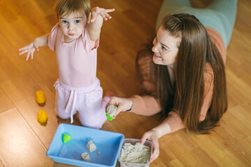 Wall Mural - A young mother and her one and a half year old daughter are sculpted from kinetic sand. Development of motor skills