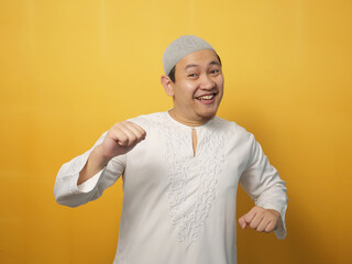 Wall Mural - Funny young Asian muslim man dancing happily joyful expressing celebrating good news victory winning success gesture, smiling positive excited emotion