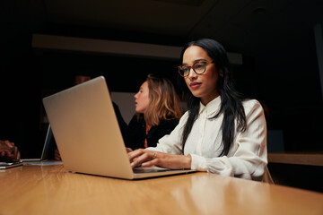 Portrait of a young businesswoman using laptop with team discussing project in the background at conference room