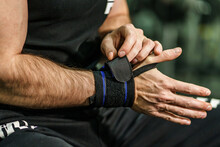 Close Up On Hands Of Unknown Man Holding And Putting On And Adjusting Wrap Bandages On Wrists For Powerlifting Body Building Training Sport Equipment At The Gym