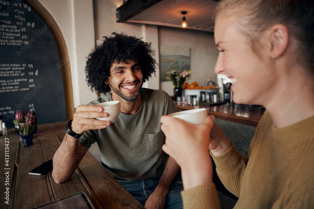 Cheerful young couple enjoying date while talking and laughing in modern cafe and drinking freshly brewed coffee - obrazy, fototapety, plakaty 