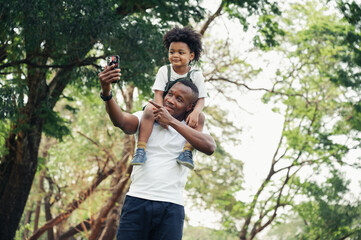 Wall Mural - happy black people father and son riding on the father back selfie in the park