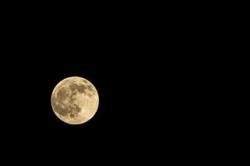 Yellow full moon in black night sky close up