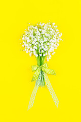 Wall Mural - bouquet of lily of the valley flowers with a bow and ribbon on a yellow background top view close up