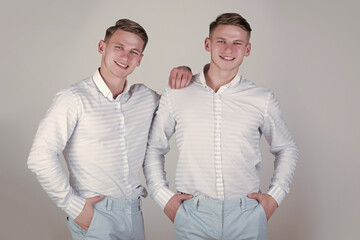 Brothers and friendship concept. Happy men hugging. Models standing together. Two brothers smiling on grey background. Twins wearing blue shirts and pants.