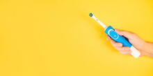 Male Hand Holding Modern Electric Toothbrush On Yellow Background. Banner, Copy Space. Controlled Oral Hygiene Tool, Ad Space.