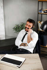 Wall Mural - Handsome man talking to the phone at his workplace. Young businessman using laptop in his office..