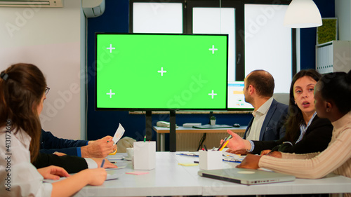 Group of business people discussing company plan with mockup tv green screen in front of desk, ready for financial project presentation. Multiethnic team using mock up monitor with chroma key display