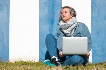 Canvas Print - Young Caucasian female sitting against a blue and white wall working on the laptop