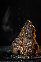 Wall Mural - American cuisine. Chef season salt on a juicy beef steak in a restaurant. in a freeze motion on black background. vertical image, place for text