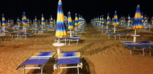 Panorama Of Empty Beach At Night With Blue And Yellow Umbrellas And Sun Loungers.
