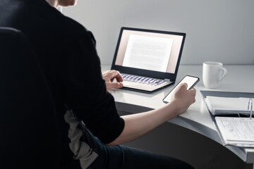 Man using phone and laptop in home office. Online college application, digital insurance, loan or mortgage document. Internet research with technology. Entrepreneur working with smartphone.