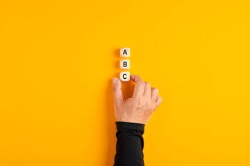 Wall Mural - Male hand placing three wooden blocks with the letters of a b and c on yellow background.