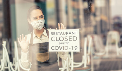 Waitress in a closed restaurant due to Covid-19 wears face mask looking out of the window