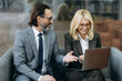 © Kateryna - Confident middle aged business partners sitting on the sofa, discussing project, smiling. Male manager and elegant female employee using laptop, searching ideas, browsing internet, teamwork concept
