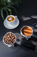 A portafilter with coffee beans, a portafilter with ground coffee, an espresso shot and an empty cup of hot coffee latte on black table.