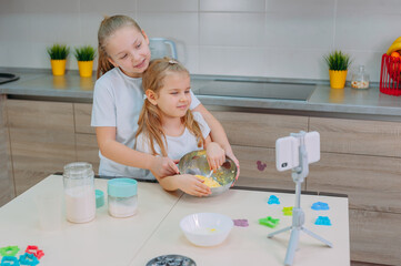 Wall Mural - Two sisters bloggers cook in the kitchen and shoot a culinary video on a smartphone.