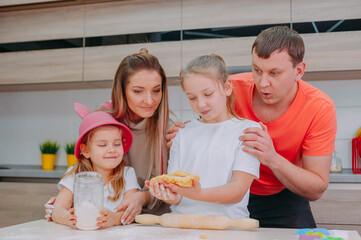 Mom with Father teaches two daughters to cook dough in the kitchen.