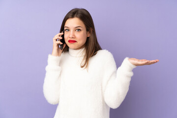 Teenager girl isolated on purple background keeping a conversation with the mobile phone with someone