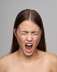 Wall Mural - Young beautiful female model close-up studio beauty portrait. Girl with natural make-up and long brunette straight hair. Crying or shouting expressive woman with closed eyes.