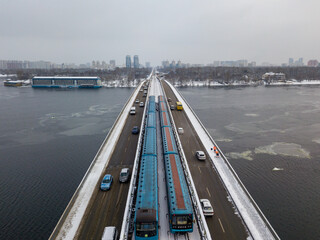 Two metro trains on a snow-covered metro bridge in Kiev. Cloudy winter morning. Aerial drone view.