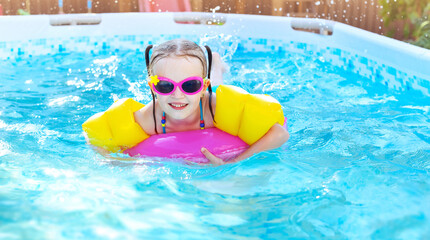 Little girl is splashing in frame swimming pool outdoor at home garden