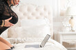 © Михаил Решетников - A sexy brunette with big breasts dressed in black underwear lies on the bed and flirts over video communication on a laptop. The woman works as a web model