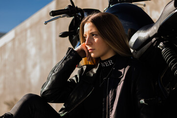 Poster - Pretty Caucasian lady wearing a leather jacket with an all-black outfit next to her motorbike