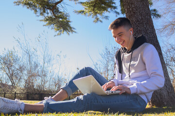 Poster - Cute Caucasian guy sitting on the grass, with his laptop on his lap and laughing