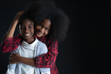 African Teen Siblings Boy And Girl Hugging With Smiley Face On Black Background. Older Sister Hug Her Younger Brother From Behind And Pat His Head. Good Family Relationship Concept