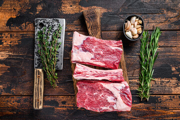 Raw beef calf short ribs meat on a butcher cutting board with cleaver. Dark wooden background. Top view