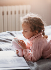 Wall Mural - Beautiful little girl lies on the bed and reads a book