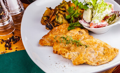 Wall Mural - Chicken schnitzel with vegetable salad and fried potatoes with mushrooms on a white plate