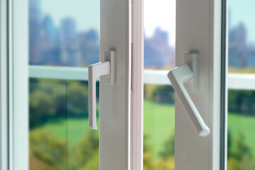 Sliding door of a balcony. Close-up of the lock on the door with and view of the city at background. White PVC door and security glass.