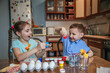 © Марина Десятниченко - Brunette brother and sister decorate Easter eggs sitting at the table at home in the kitchen.