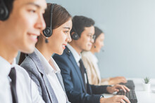 Asian Call Center Team, Customer Service, Telesales In Formal Suit Wearing Headset Or Headphone Talking With Customer In Modern Office