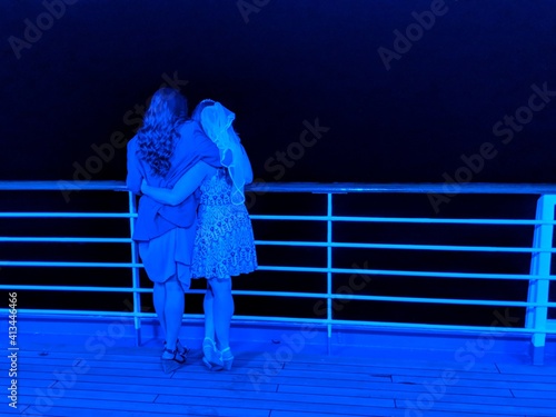 Rear View Of Friends Standing On Boat Deck In Blue Neon Light At Night