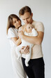 © shunevich - A beautiful married couple, with a little daughter, are photographed in the studio against a background of business. Caring parents look at their baby, holding her in their arms.