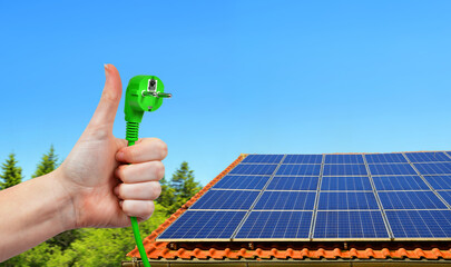 Wall Mural - solar energy panel on the roof of the house and hand holding green electric plug in sunny day. conce