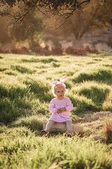 Wall Mural - Baby girl wears rabbit ears, sitting in grass.