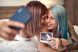 © luckybusiness - A young happy lesbian couple taking a selfie with ultrasound photo showing their baby. Love, pregnancy, lgbt, relationship