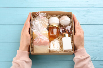 Woman holding box with stylish craft gift set at light blue wooden table, top view