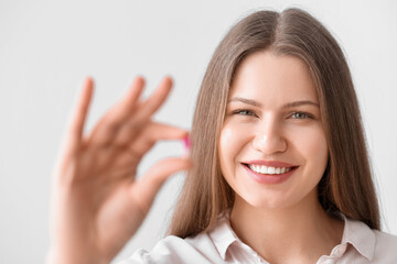 Poster - Beautiful young woman with pill on light background