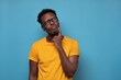 Young african man in glasses thinking over blue background. Studio shot