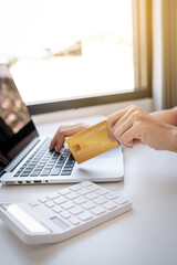 Young Asian consumer woman hand holding a credit card, Ready to spending pay online shopping according to discount products via smartphone and laptop from home