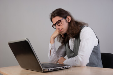 bored student is sitting at a laptop. Guy is a geek gamer, uses a laptop. Uninteresting course, boredom and procrastination.