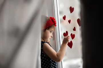 Little girl with small red paper hearts near the window.